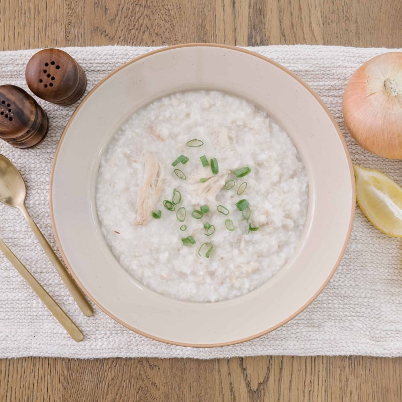 Bowl of healing postpartum chicken and rice with garnishes on a wooden table