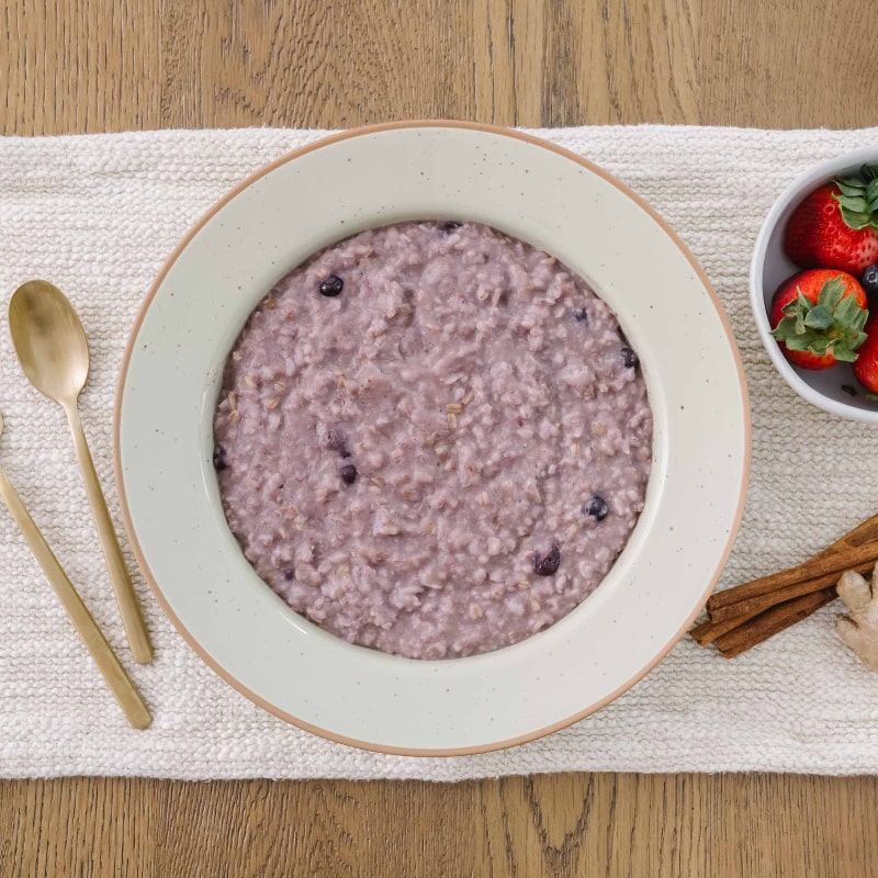 Bowl of purple postpartum porridge with berries that is organic and regenerative and gluten-free