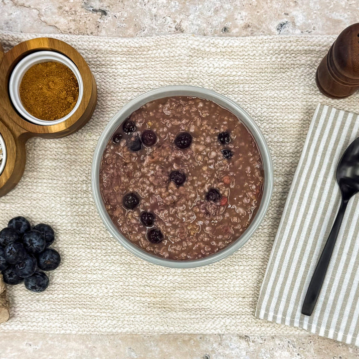 Very Berry Oatmeal Congee in a bowl with fresh blueberries and spices alongside