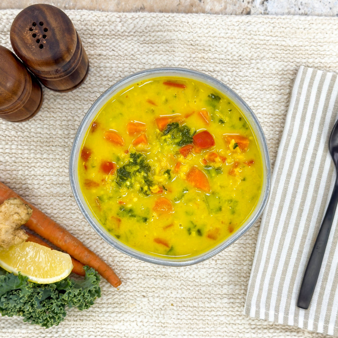 Golden red lentil soup with carrots and broccoli beside fresh kale, lemon, and ginger