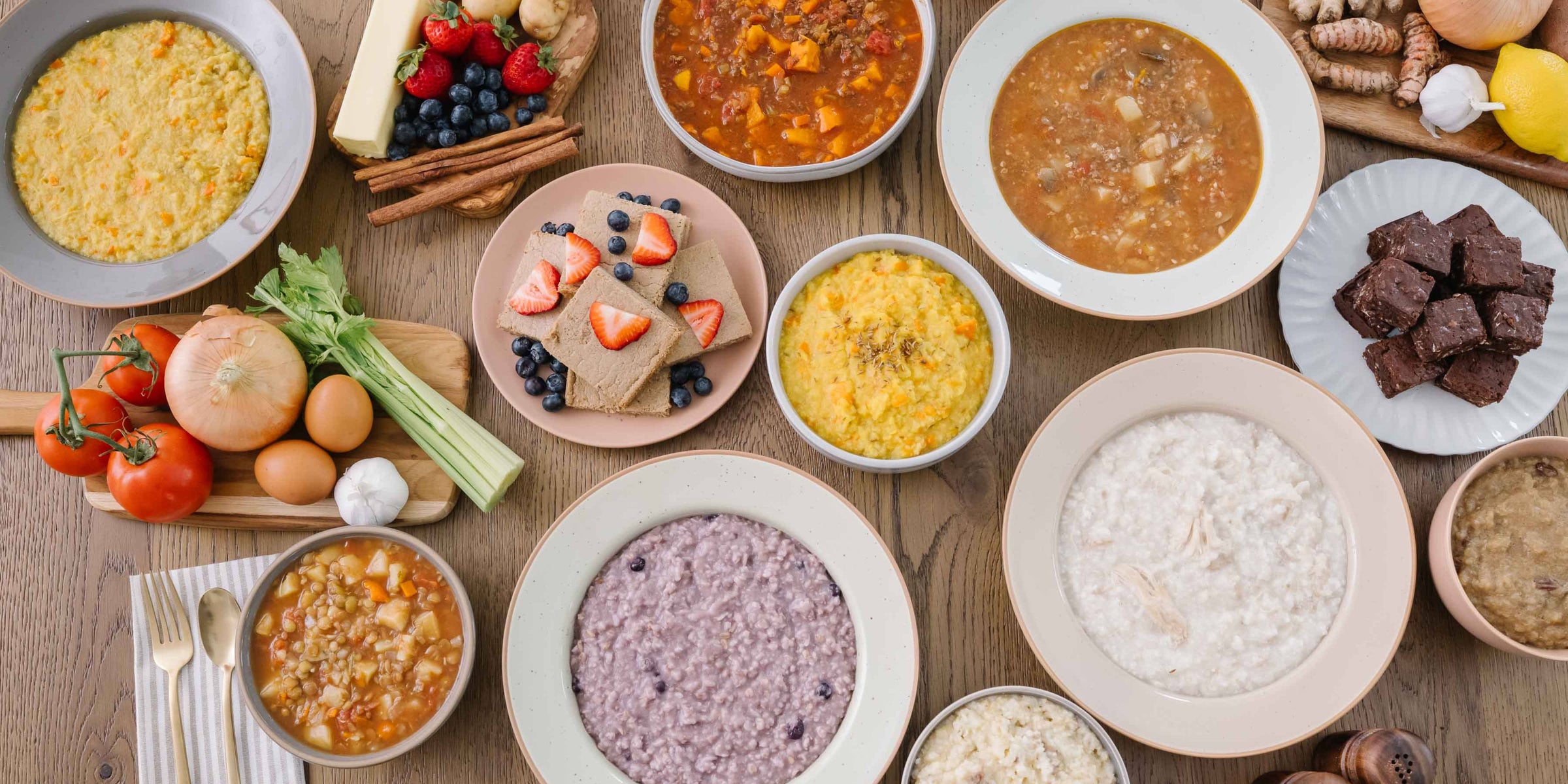 Assorted postpartum foods including soups, fruits, and pancakes on a wooden table