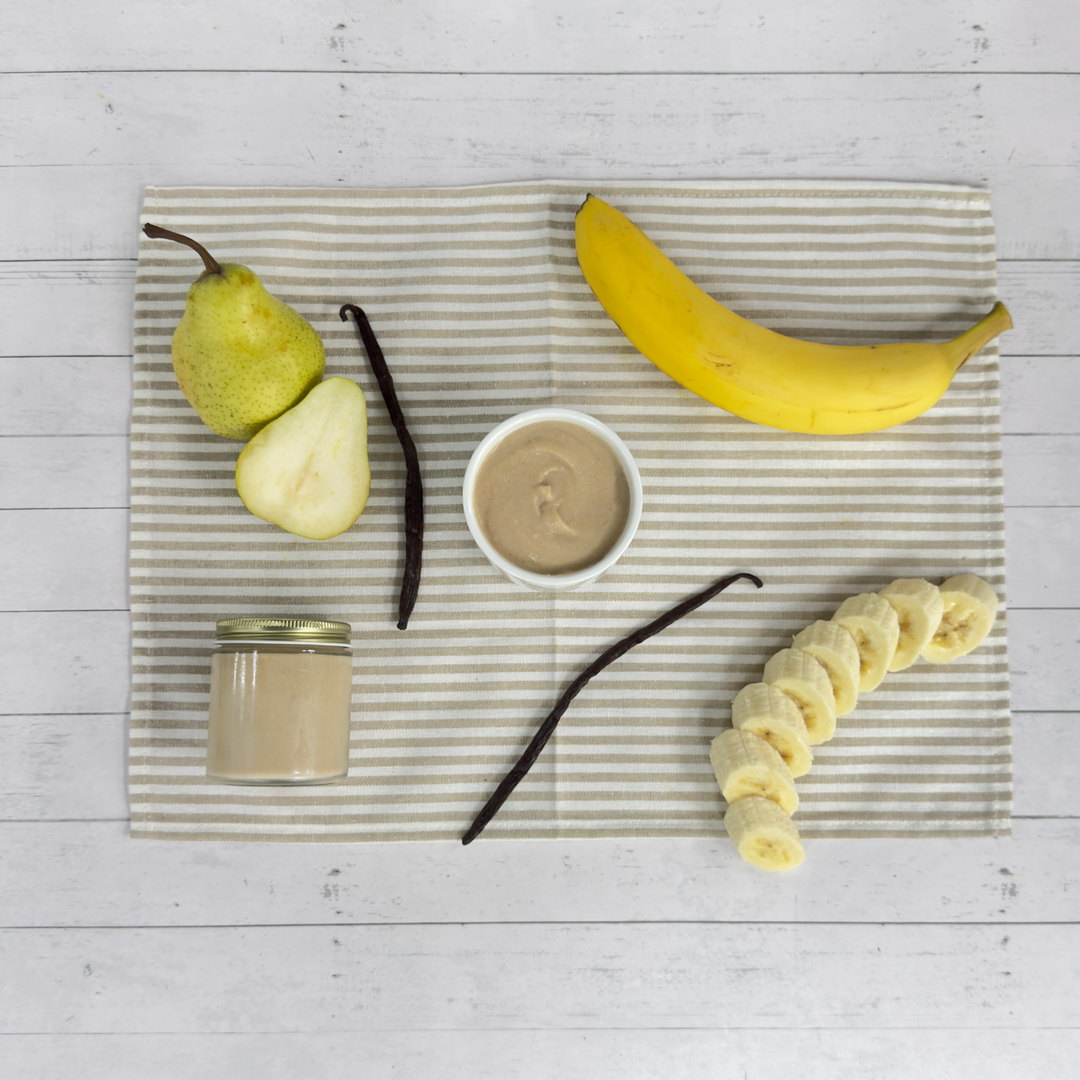 Jars of creamy banana pear puree with fresh banana, pear, and vanilla beans on striped linen