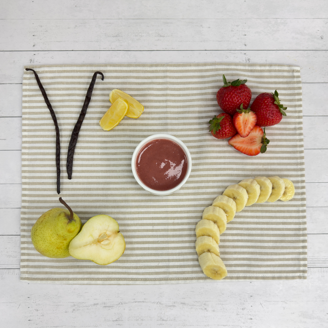 Bowl of berry puree with fresh strawberries, banana slices, pear, and vanilla bean on striped linen