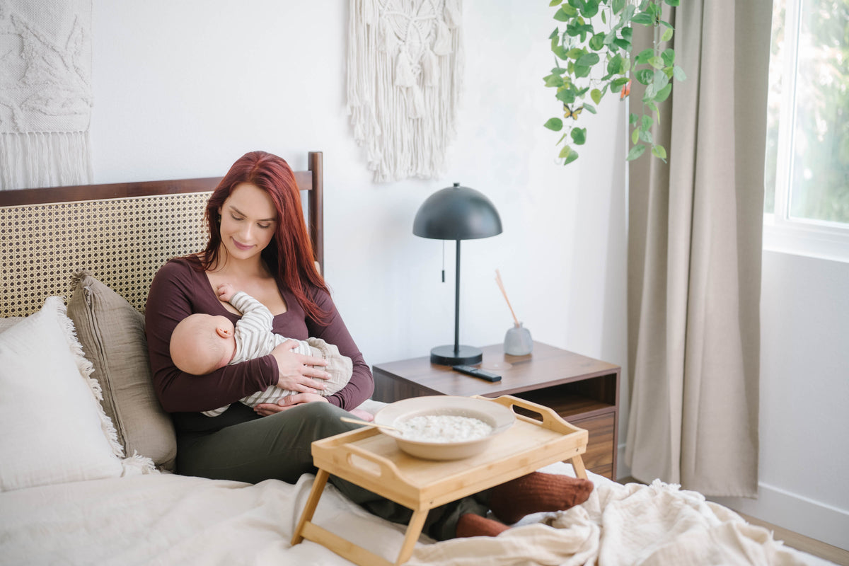 Mother nursing her baby in bed beside a breakfast tray